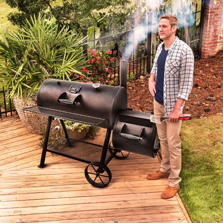 A person standing next to an offset smoker, with smoke coming out of it