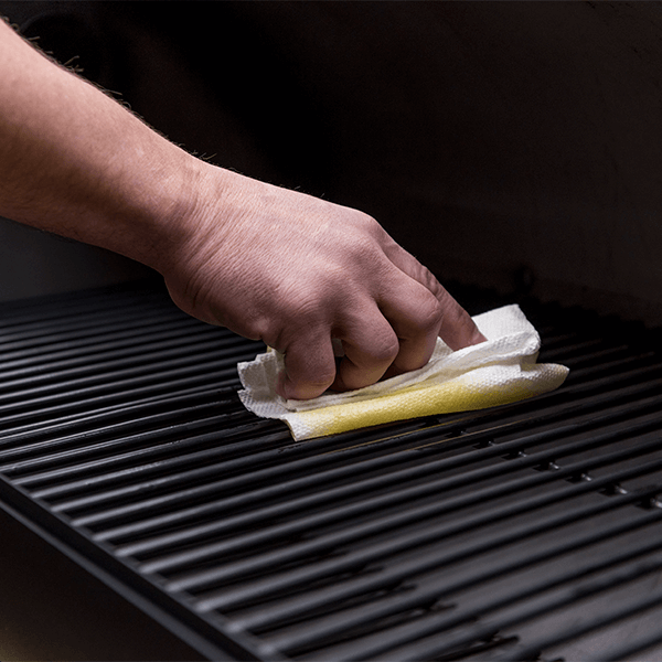 A person preparing a cooking chamber of a smoker grill by cleaning it