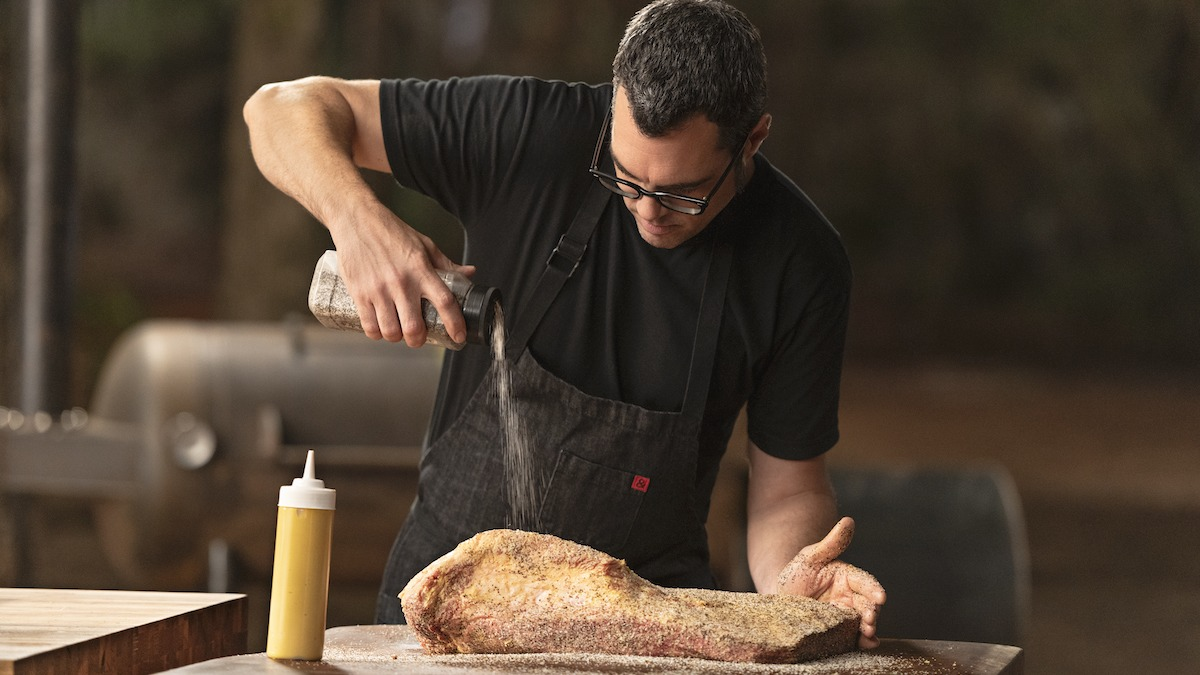 Aaron Franklin adding a dry rub to a piece of meat